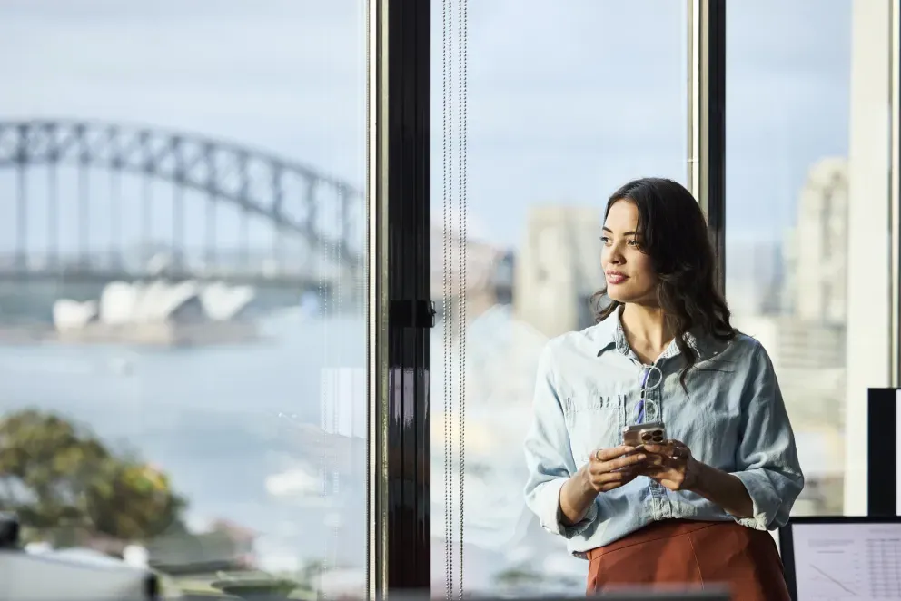 Woman sitting by large windows with Sydney Harbour Bridge visible in background