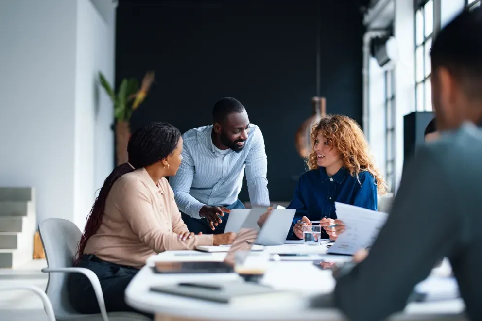 Three colleagues collaborating around a table in a modern office, reviewing documents together.