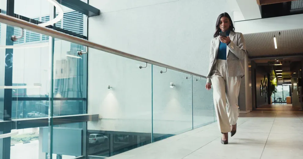Professional woman in a beige suit walking confidently through a modern office corridor.