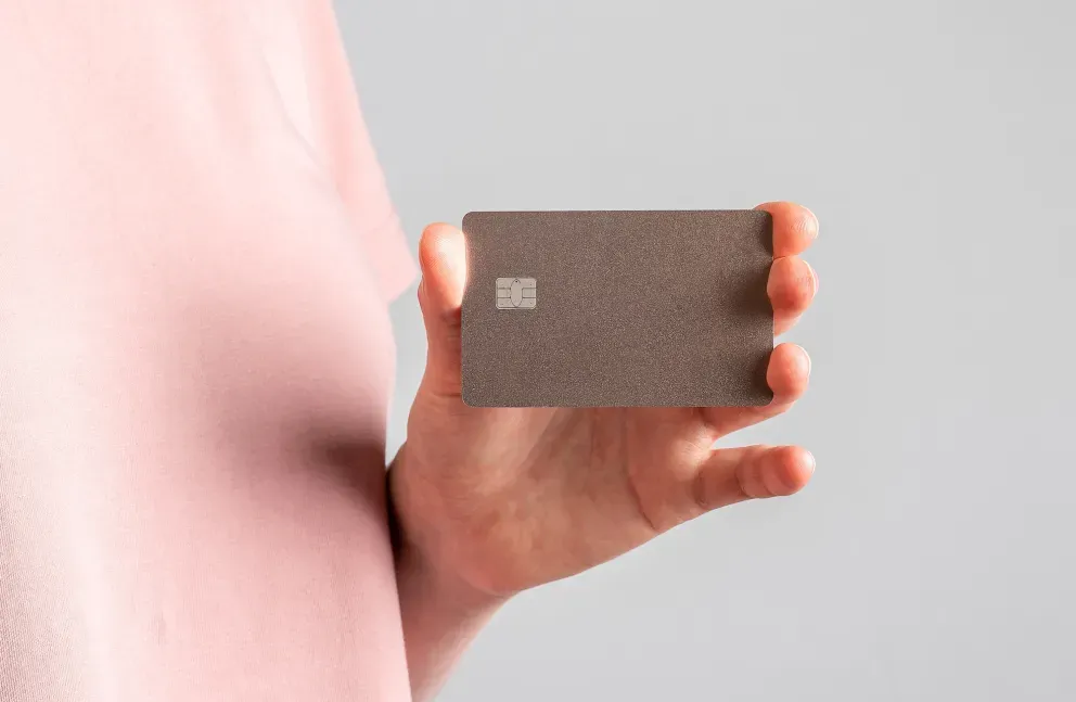 Hand holding a metallic gray credit card against a light gray background. Hand holding a metallic gray credit card against a light gray background.