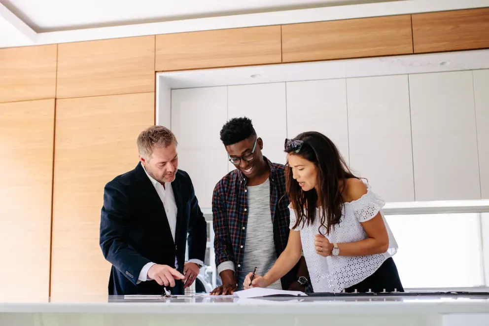 Three people collaborating over documents on a white table in a modern office setting. Three people collaborating over documents on a white table in a modern office setting.