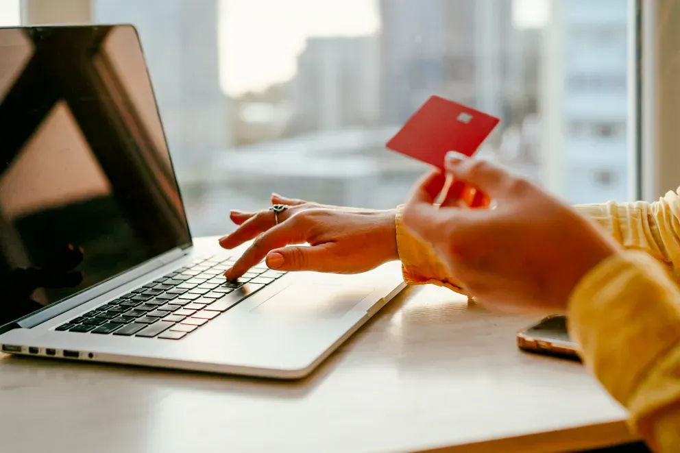 Person holding a red credit card while typing on a laptop, online shopping concept.