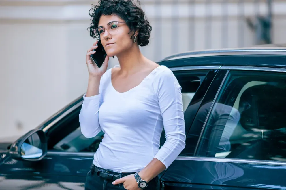 Woman in white top talking on the phone against a black car