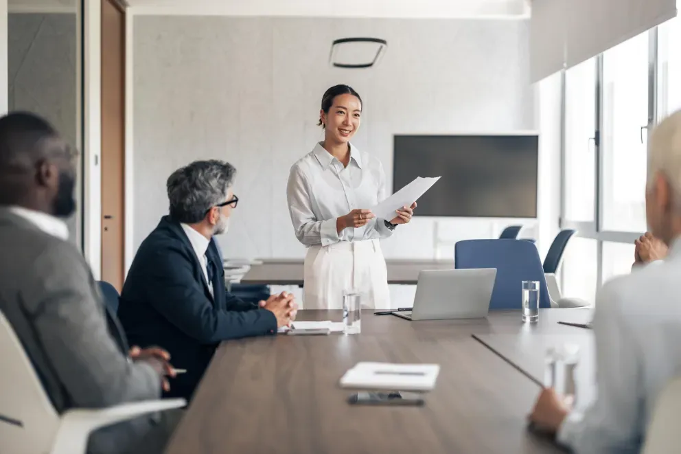 Smiling businesswoman presenting documents to colleagues in a modern conference room.