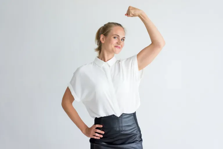 Woman in white blouse flexing her arm muscle confidently against a light gray background. Woman in white blouse flexing her arm muscle confidently against a light gray background.
