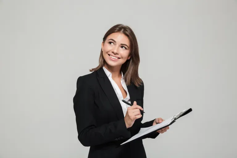 Woman in black blazer holding clipboard and pen, looking up thoughtfully.