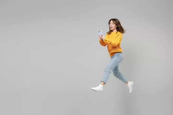 woman smiling leaping with cell phone in hand