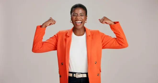 Woman in orange blazer smiling and curling arms in a position showing strength