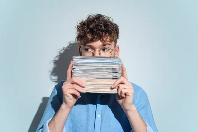 man hiding behind a stack of papers