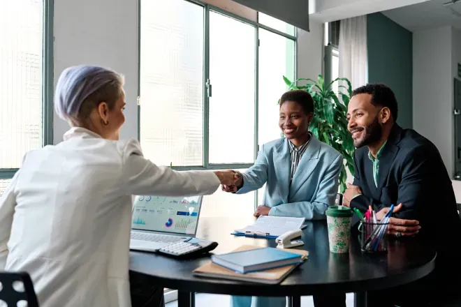 Three people collaborating around a laptop in a bright modern office with large windows. Three people collaborating around a laptop in a bright modern office with large windows.
