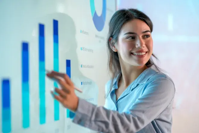 Young woman smiling while pointing at a glowing blue bar chart presentation. Young woman smiling while pointing at a glowing blue bar chart presentation.