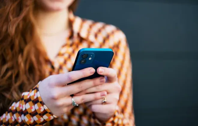 Young woman with red hair in a striped top, looking at a blue smartphone. Young woman with red hair in a striped top, looking at a blue smartphone.