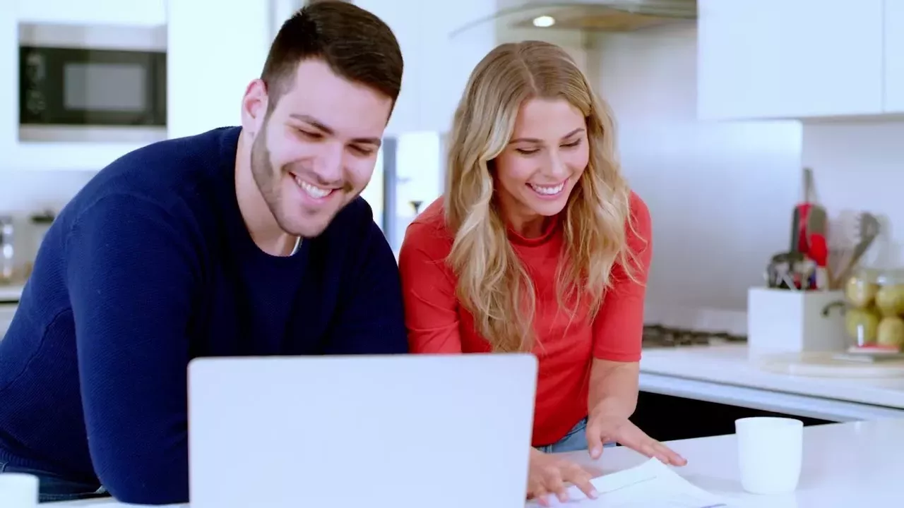 two people looking at computer in kitchen two people looking at computer in kitchen
