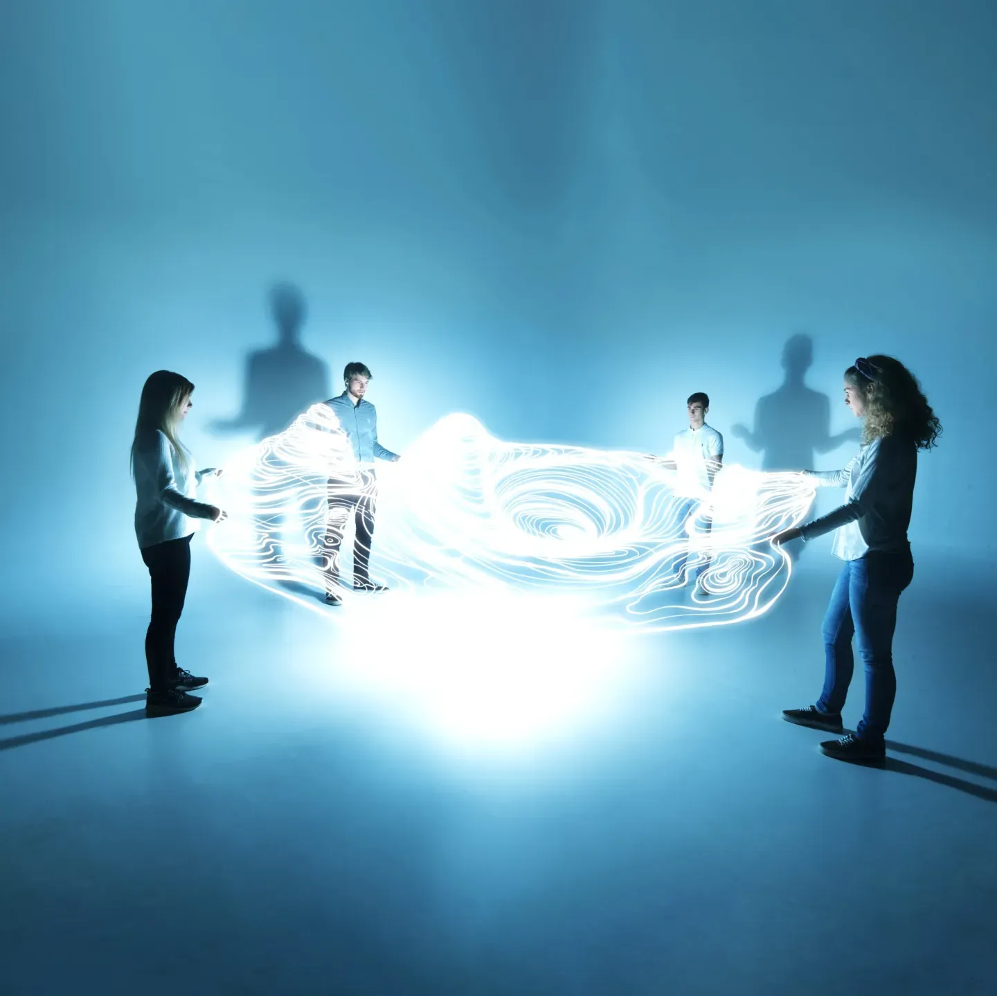 Four silhouetted figures surrounding a glowing blue swirling light energy in a dark room. Four silhouetted figures surrounding a glowing blue swirling light energy in a dark room.
