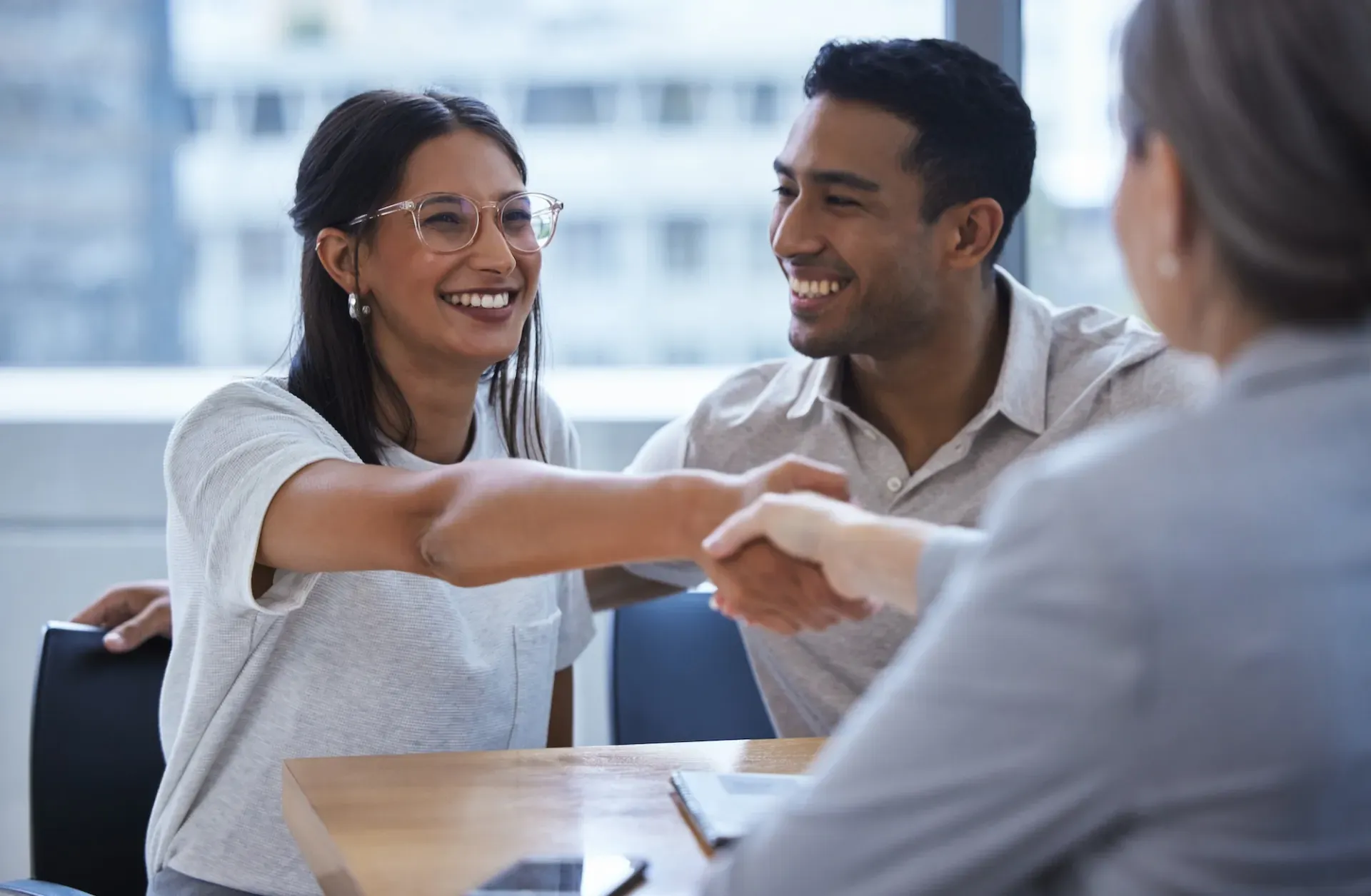 Smiling couple shaking hands with a professional during a meeting in a bright office.