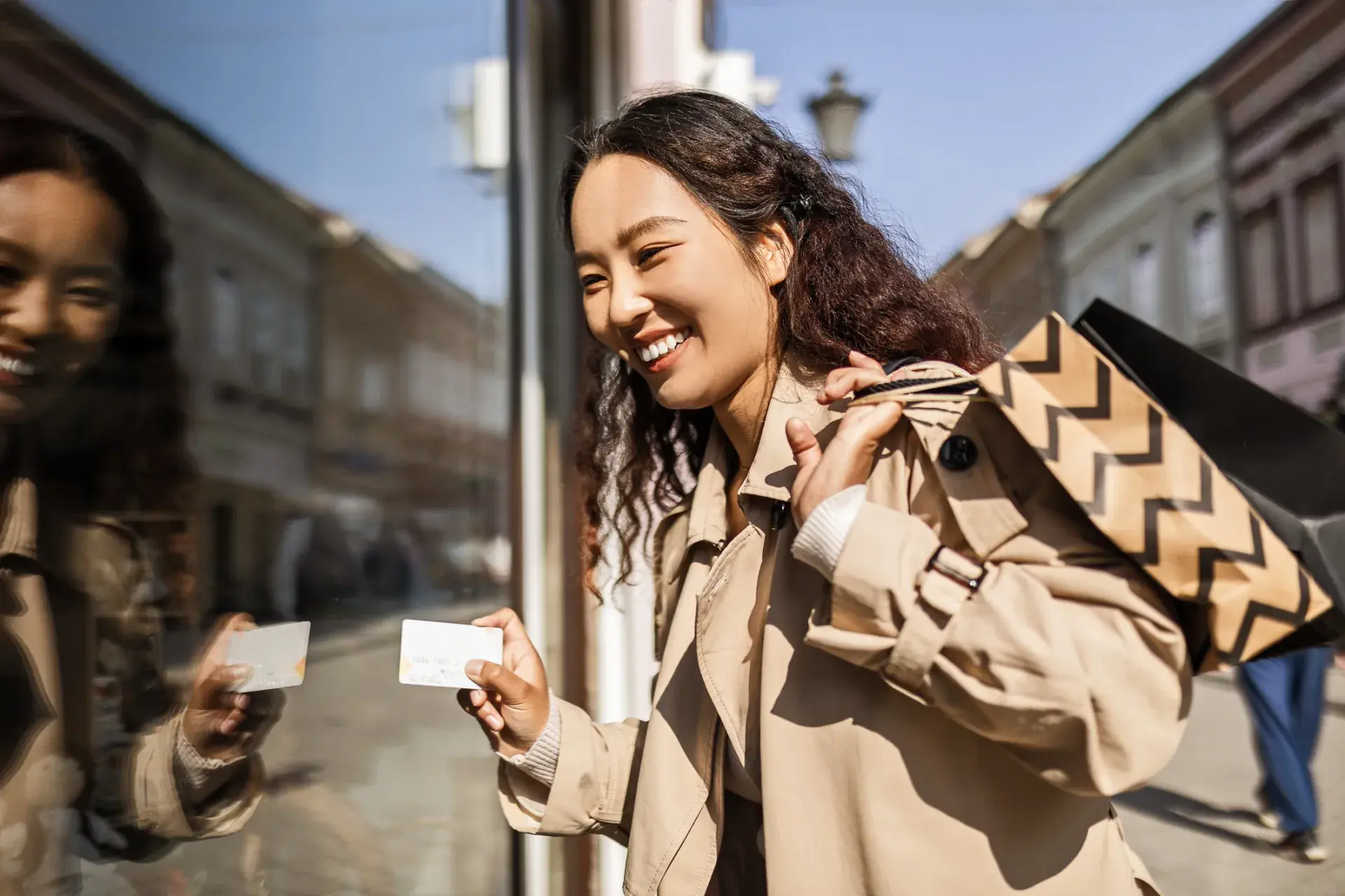 woman holding shopping backs and a credit card next to a window with her reflection